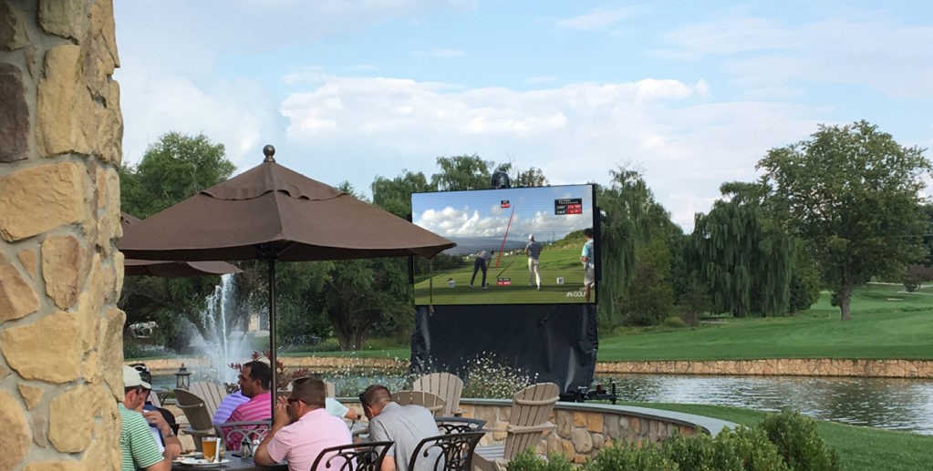 Golf club displaying digital scoreboard and LED scoreboard in background while golfers eating 
